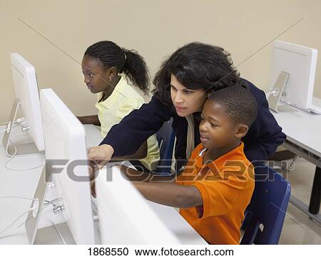 Stock Image - teacher helping a student with the computer. Fotosearch