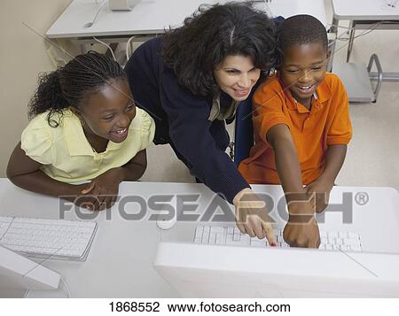 Stock Image - teacher working with students in computer class. Fotosearch