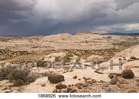 Stock Photograph - utah, united states of america; desert storm with lava boulders in the foreground at grand staircase-escalante national monument. Fotosearch