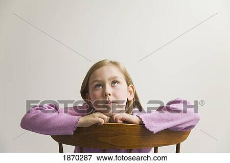 Stock Photo - young girl sitting on a wooden chair looking up. Fotosearch