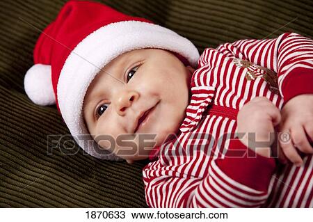 Stock Image - a baby wearing a red and white christmas sleeper and a santa hat. Fotosearch