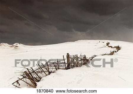 Stock Image - a broken fence in a snowy field with a dark sky above. Fotosearch