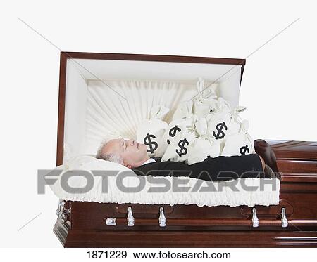 Stock Photo - a deceased man in a coffin surrounded by bags of money. Fotosearch