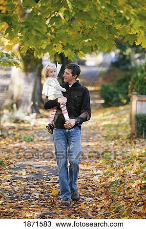 Stock Image - a father holds his daughter while walking down a sidewalk in autumn. Fotosearch