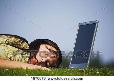 Stock Photograph - a girl who has fallen asleep on her laptop computer while working in the park. Fotosearch