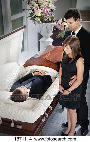 Picture - a man and a woman viewing a body in a coffin. Fotosearch