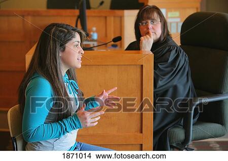 Picture - a teenage girl giving her testimony before a judge. Fotosearch
