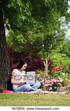 Picture - a teenage girl working on her laptop computer under a tree. Fotosearch