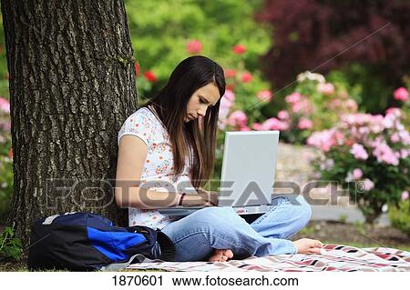 Stock Image - a teenage girl working on her laptop computer under a tree. Fotosearch