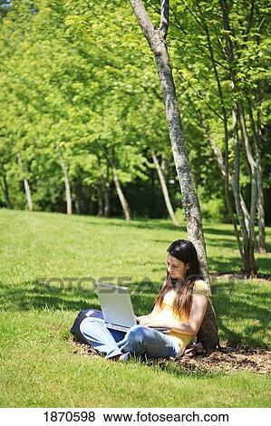 Stock Photo - a teenage girl working on her laptop under a tree. Fotosearch