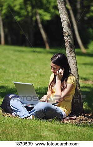 a teenage girl working on her laptop and talking on her cellphone under a tree View Large Photo Image Stock Photo - a teenage girl working on her laptop and talking on her cellphone under a tree. Fotosearch