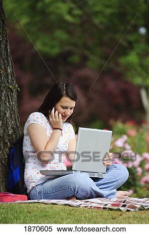 a teenage girl working on her laptop computer and talking on her cellphone under a tree View Large Photo Image Stock Photography - a teenage girl working on her laptop computer and talking on her cellphone under a tree. Fotosearch