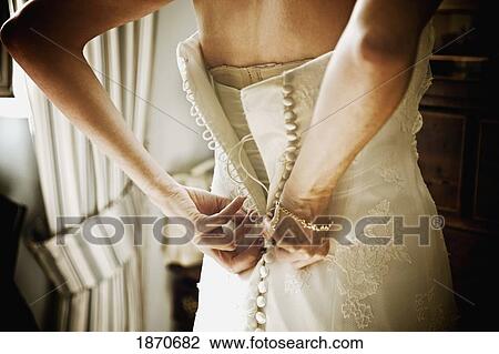 Stock Image - a woman buttoning up the back of her white wedding dress. Fotosearch