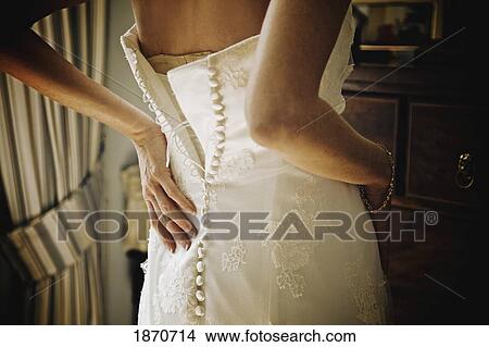 a woman fastening the back of her wedding dress View Large Photo Image Picture - a woman fastening the back of her wedding dress. Fotosearch