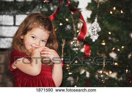a young girl holds an ornament as she stands by the christmas tree View Large Photo Image Stock Image - a young girl holds an ornament as she stands by the christmas tree. Fotosearch