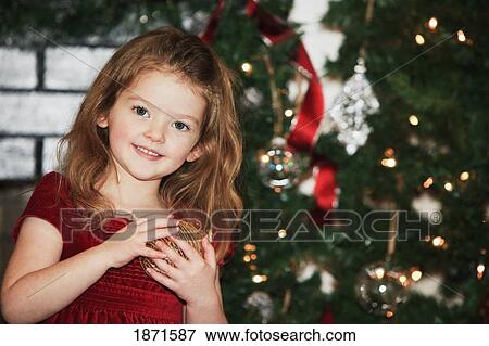 a young girl holds an ornament as she stands by the christmas tree View Large Photo Image Stock Photo - a young girl holds an ornament as she stands by the christmas tree. Fotosearch