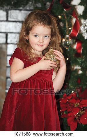 Stock Photo - a young girl holds an ornament as she stands by the christmas tree. Fotosearch