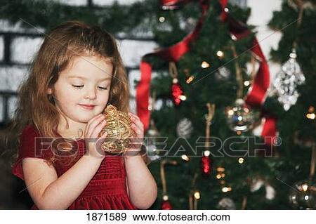 a young girl holds an ornament as she stands by the christmas tree View Large Photo Image Stock Photo - a young girl holds an ornament as she stands by the christmas tree. Fotosearch