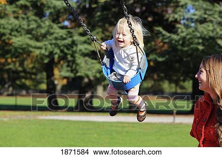 a young girl in a swing as her mother watches View Large Photo Image Picture - a young girl in a swing as her mother watches. Fotosearch