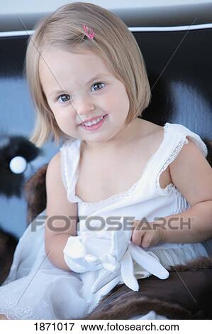 Stock Photo - a young girl wearing a white dress and putting on white gloves. Fotosearch