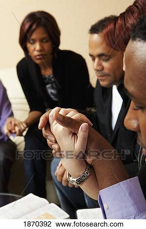 Stock Image - adults praying together with their bibles open. Fotosearch