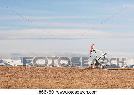Stock Image - alberta, canada; pump jack in a brown field with snow covered mountains in the background. Fotosearch