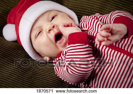 Stock Image - an infant wearing a red and white christmas sleeper and a santa hat. Fotosearch