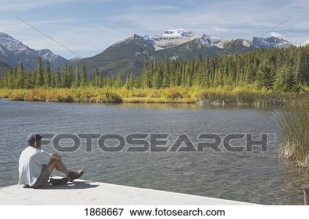 Stock Photo - banff national park, alberta, canada; a man sitting on a dock at vermilion lakes. Fotosearch