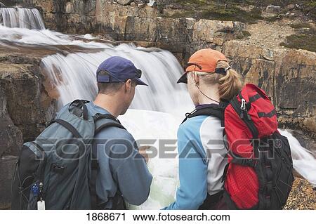 Stock Image - lake louise, alberta, canada; a couple hiking and looking at a map next to the waterfall at giant steps. Fotosearch