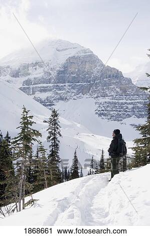 Stock Image - lake louise, banff national park, alberta, canada; a man snowshoeing on a trail looking at the snow-covered mountains. Fotosearch