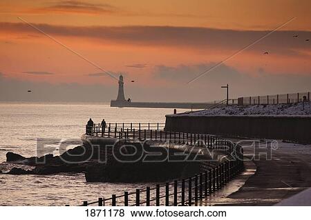 Stock Photo - sunderland, tyne and wear, england; people walking along the coast with a lighthouse in the distance. Fotosearch