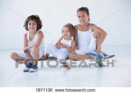 Stock Image - three young girls sitting on a longboard. Fotosearch