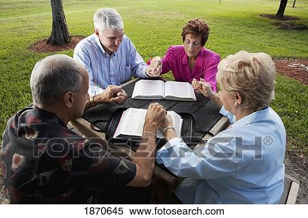 Stock Photography - two couples meeting in the park with their bibles and praying. Fotosearch