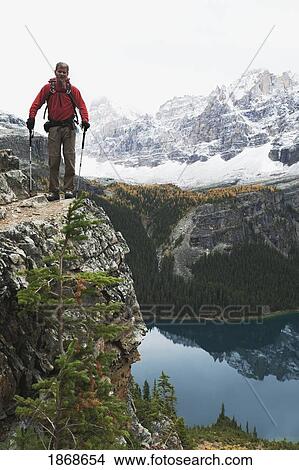 yoho national park, british columbia, canada; a male hiker standing on a cliff overlooking lake o'hara in autumn View Large Photo Image Picture - yoho national park, british columbia, canada; a male hiker standing on a cliff overlooking lake o'hara in autumn. Fotosearch