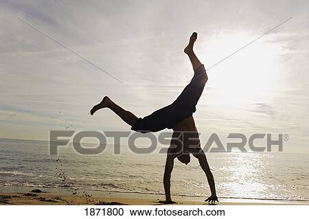 Stock Image - young man doing a cartwheel on the beach. Fotosearch