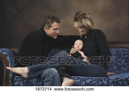 Picture - a family sitting on a couch holding their baby. Fotosearch
