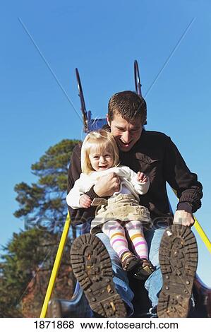 Stock Photo - a father and daughter going down a slide together at a playground. Fotosearch