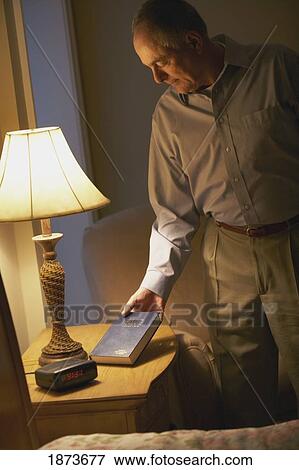 Stock Photo - a man putting a bible on the night stand. Fotosearch