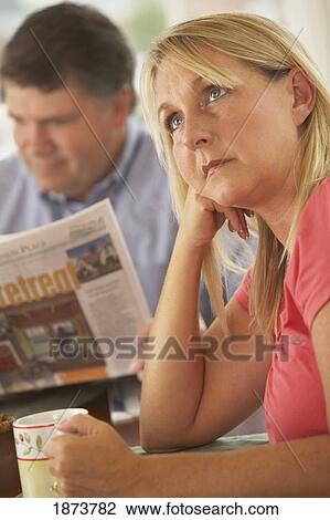 Stock Image - a wife ignored by a husband reading the newspaper. Fotosearch