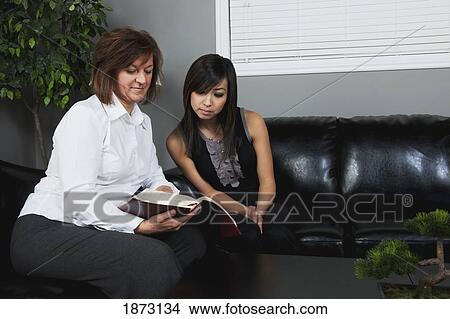 Picture - a woman showing a passage from the bible to a young woman. Fotosearch