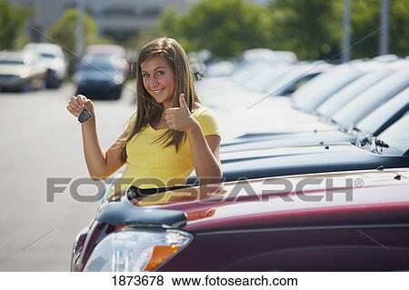 Stock Photo - a young woman with keys to a vehicle in a car dealership. Fotosearch
