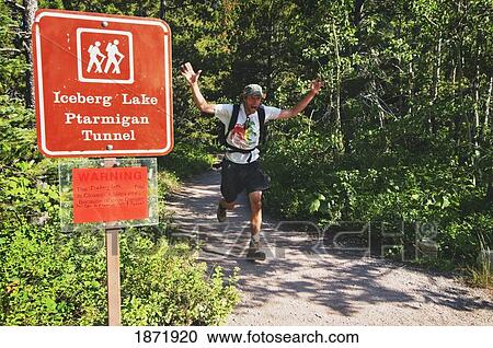 Stock Image - glacier national park, montana, united states of america; a hiker running down the trail passing a grizzly bear warning sign. Fotosearch
