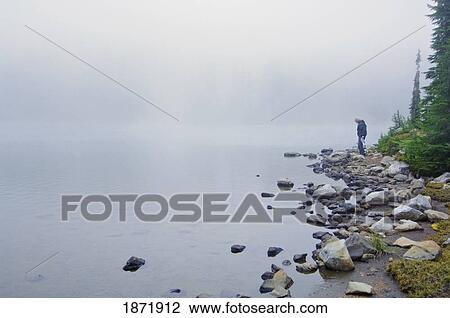 Stock Image - mount jefferson, oregon, united states of america; a man standing on the rocks at the shore of russell lake. Fotosearch
