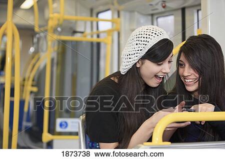 Stock Photo - portland, oregon, united states of america; two teenage girls using a cell phone while sitting on public transportation. Fotosearch