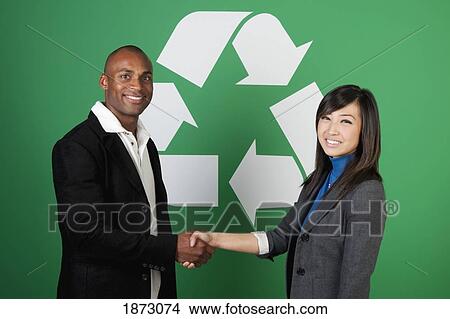 Picture - two business people shaking hands in front of a recycle symbol. Fotosearch