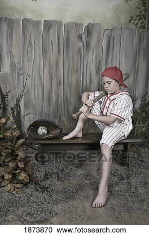 a boy holding a baseball bat and wearing a uniform sitting on a bench View Large Photo Image Stock Image - a boy holding a baseball bat and wearing a uniform sitting on a bench. Fotosearch