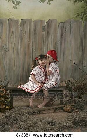 Stock Photo - a boy whispering to a girl wearing matching baseball uniforms. Fotosearch
