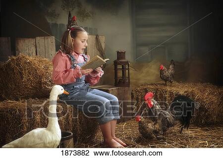 Stock Image - a girl reading a story book to animals in the barn. Fotosearch