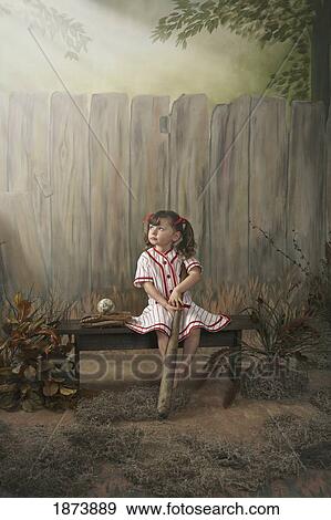 Stock Photo - a girl sitting on a bench wearing a vintage girl's baseball uniform. Fotosearch