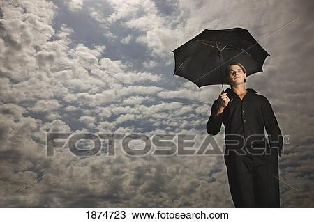 a man holding an umbrella under a sky filled with clouds View Large Photo Image Stock Image - a man holding an umbrella under a sky filled with clouds. Fotosearch